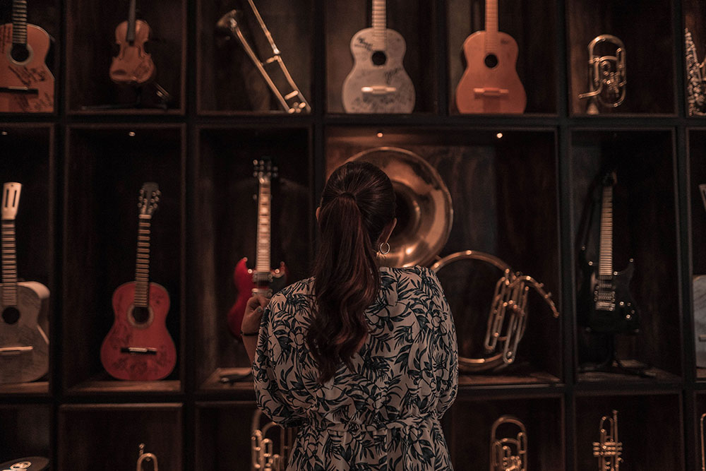 Eine Frau steht vor einer Vitrine, in der Instrumente ausgestellt sind. Gitarren, Posaunen, Tuben und Trompeten