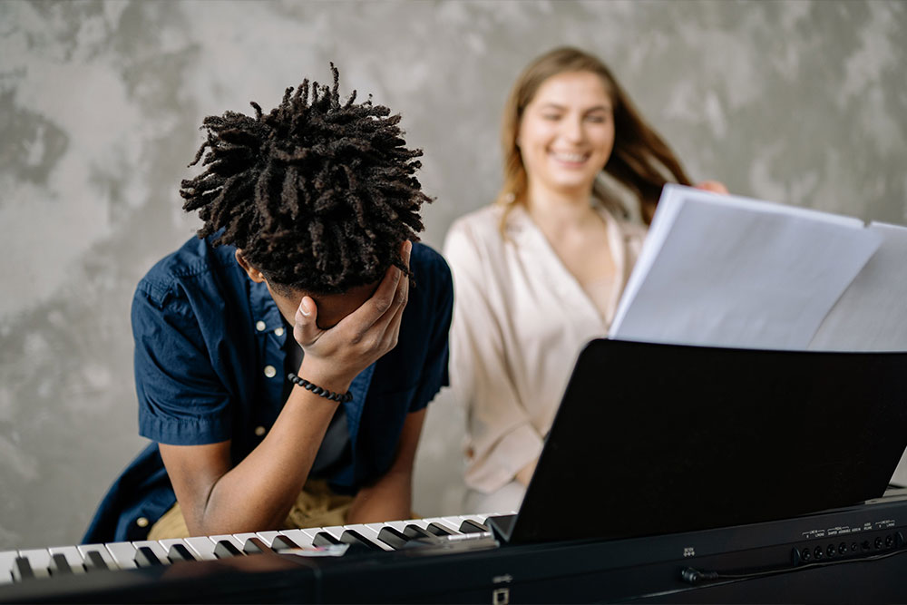 Ein junger Pianist und seine Klavierlehrerin lachen während einer Unterrichtseinheit